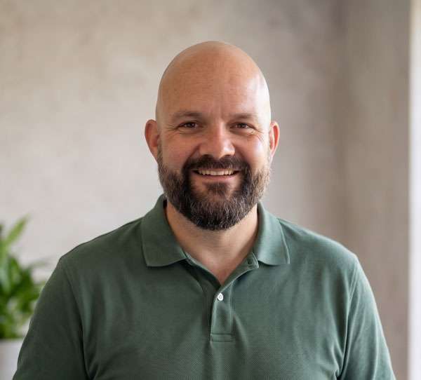 MarkProfileCropped2 Bald man with beard in green polo shirt smiling